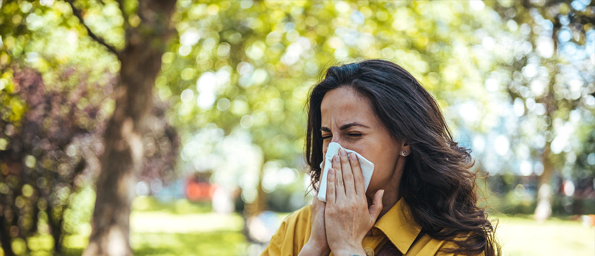 woman blowing nose under trees