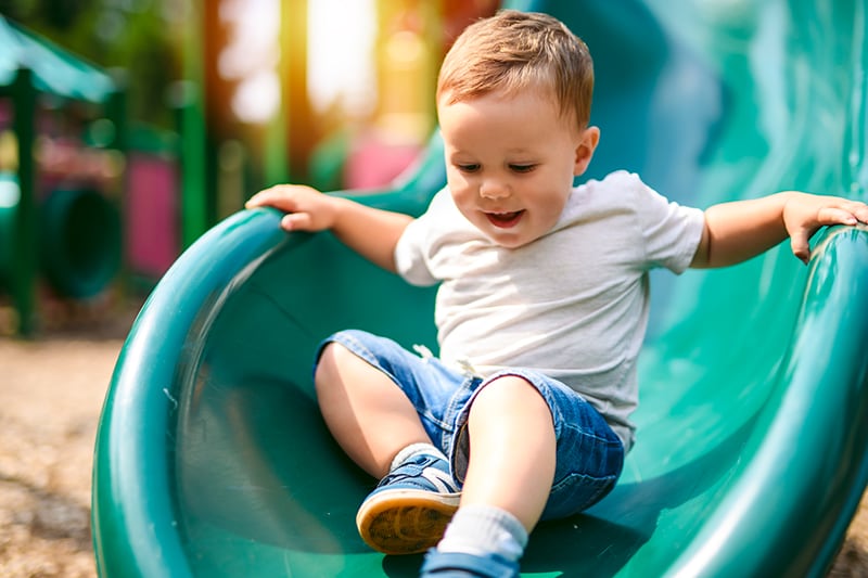 Child sitting at the top of a playground slide