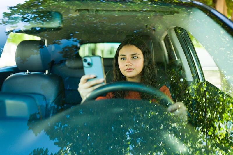Teenage girl looks at mobile phone while sitting in the driver's seat
