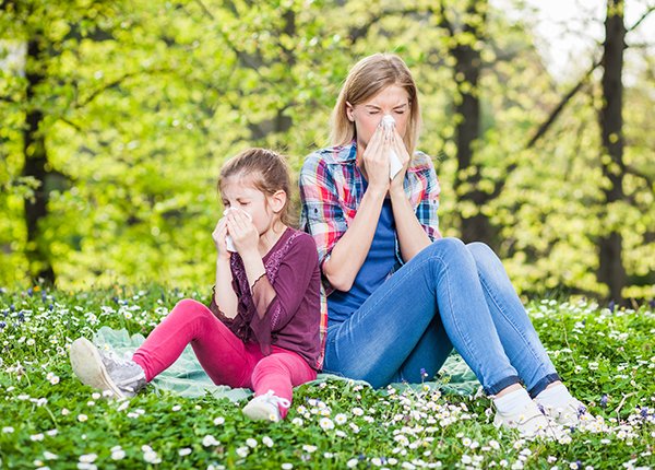 Two women sitting outdoors sneezing